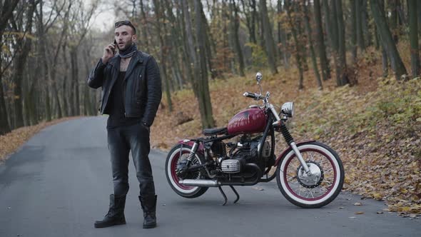 Brutal Man Uses Smartphone in Autumn Park at Motorbike alt