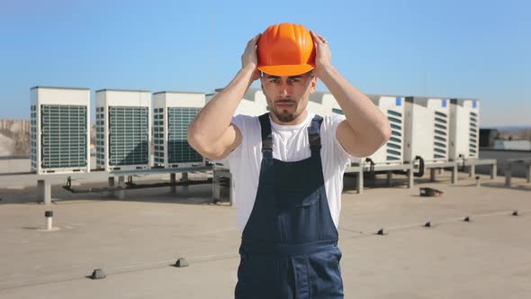 Portrait of a Young Engineer Who is Putting a Protective Helmet on His Head alt