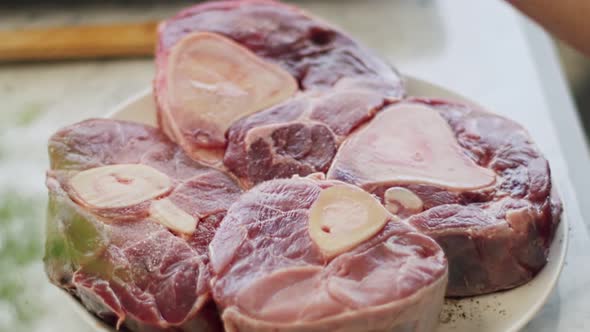 Woman grinding spices on raw beef shank in kitchen alt