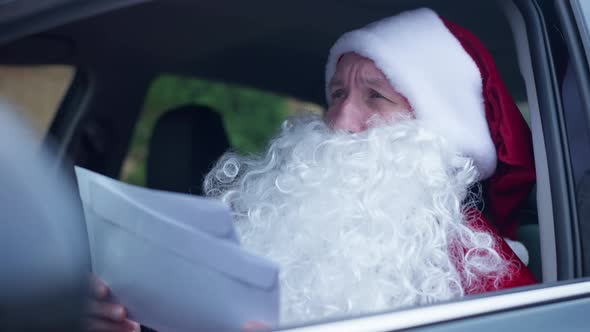 Busy Santa Clause Sitting in Car Reading Letters Envelopes Looking Around alt
