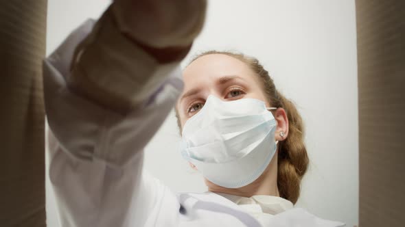 Young Woman Doctor Wearing Medical Mask and Gloves Putting Medicine Into Box alt