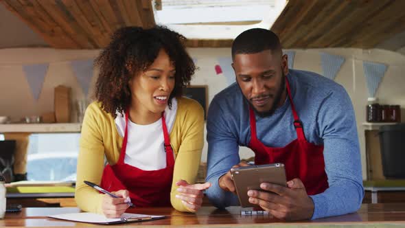 African american couple smiling while using digital tablet in food truck alt