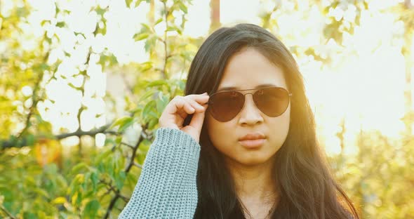 Asian Model in Sunglasses Looking at Camera with Sunset on Background