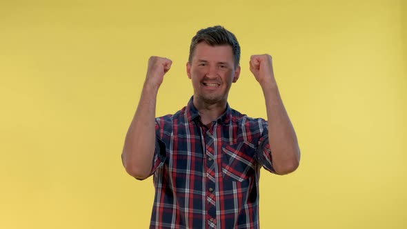 Excited Young Man Yelling and Raising Fists in Cheer on Yellow Background alt