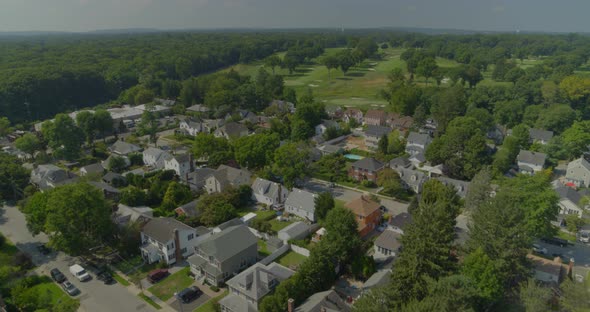 Flying Over Suburban Homes and Towards Golf Course Near Forest in Long Island alt