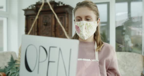 Young Woman Florist Closing Her Flower Store Due to Pandemic Lockdown Viewed Through Glass Door alt
