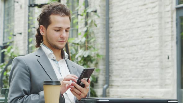 A young successful businessman is working outdoor using smartphone. alt