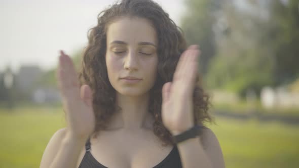 Close-up Portrait of Confident Brunette Curly-haired Woman Putting Hands Together, Closing Eyes alt