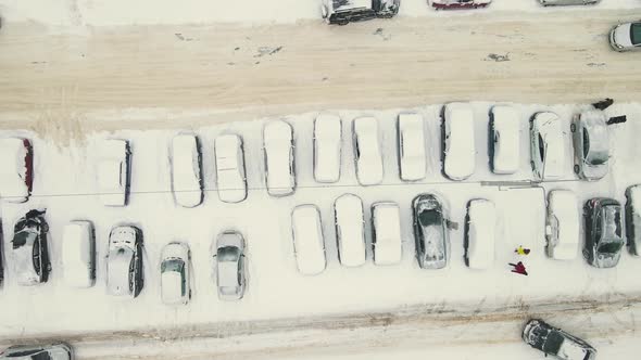 Cars Stand in a Row Covered with Snow After a Blizzard and Drive Along the Road alt