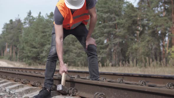 A Railway Man in a Helmet Repairs a Railway, Hammering the Spire with a Sledgehammer	 alt