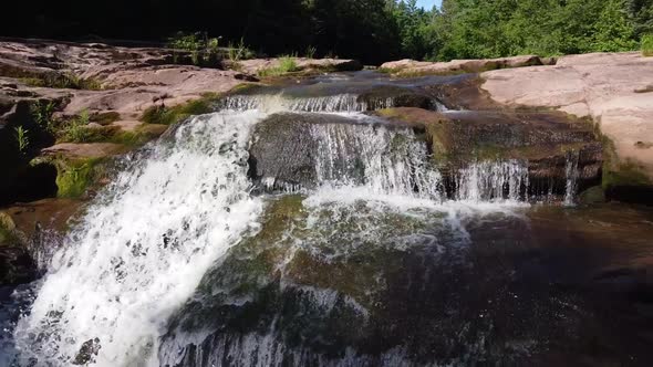 Aerial Backwards Over River with Brown Rocks Leading to Serene Waterfall alt