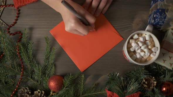 A Woman's Hands Writing a Christmas Card with a Pen Surrounded By Christmas Decorations alt