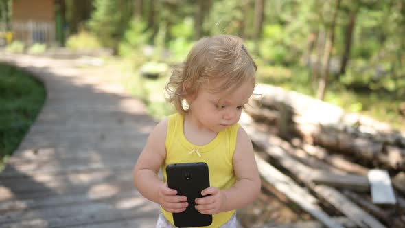 Little Funny Cute Blonde Girl Child Toddler Holding Playing Big Black Smartphone Outside at Summer
