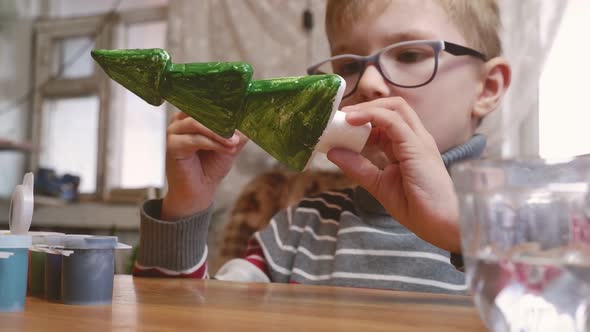 A Sevenyearold Boy Paints a Styrofoam Christmas Tree Green in Preparation for Christmas alt