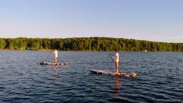 Two Friends Smoothly Sail Away From the Shore of the Lake and Row with Oars alt