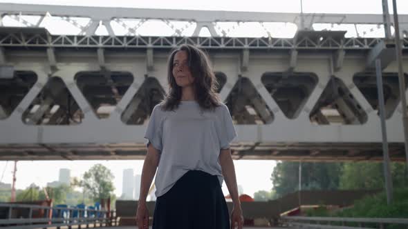the Brunette Walks Slowly and Touches Hair Against the Background of the Railway Bridge alt