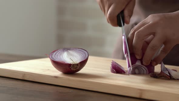 Professional chef slicing red onion with knife on wood cutting board