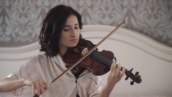 Beautiful Girl Playing the Violin While Sitting on the Bed at Home