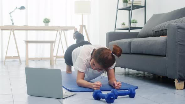 Young lady exercises doing working out and using laptop to watching yoga video tutorial at home. alt
