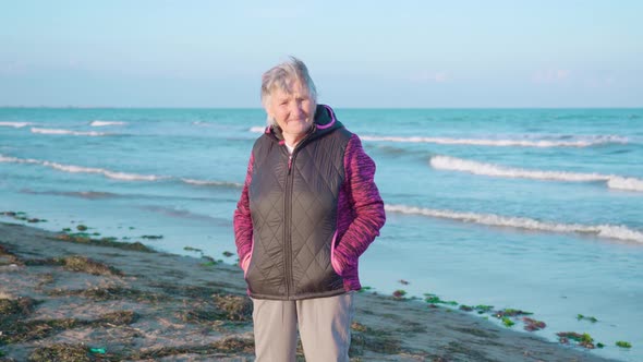 Elderly Woman Stands on Wet Sand Beach Enjoying Weather alt