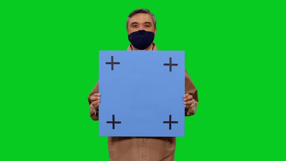 Adult Man in Mask Moving Towards the Camera with Blue Blank Board in Hands, Chroma Key