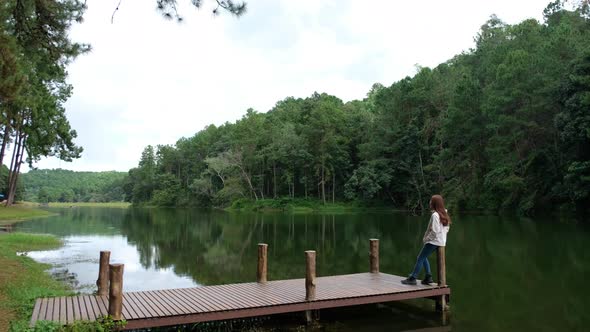 A female traveler waving hand while sitting on wooden dock by the lake