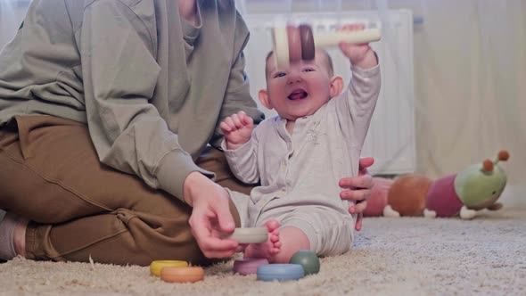 A happy child and mother play with a pyramid on the carpet in the home room, age eight months.