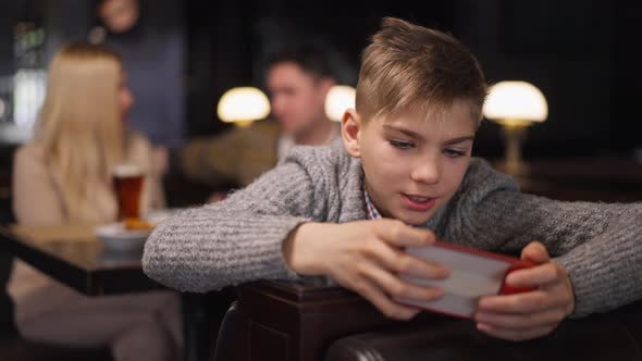 Absorbed Teenage Boy Gesturing Victory in Slow Motion Gaming Online on Smartphone alt