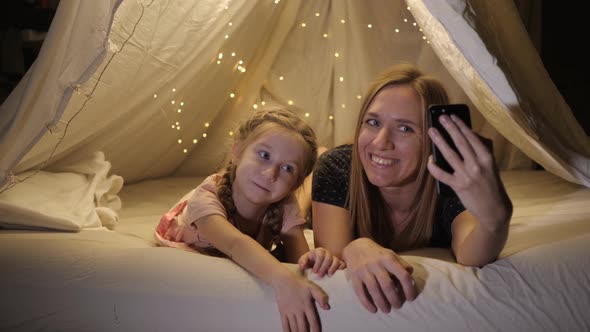 Happy Mother and Daughter Are Photographed on the Phone in a Makeshift Tent