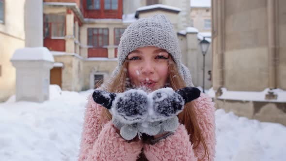 Young Woman Traveler Tourist Showing Snow in Hands Palms To Camera and Blowing It on City Street alt