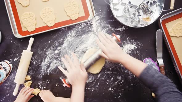 Flat lay. Mother and daughter baking sugar skull cookies for Dia de los Muertos holiday. alt