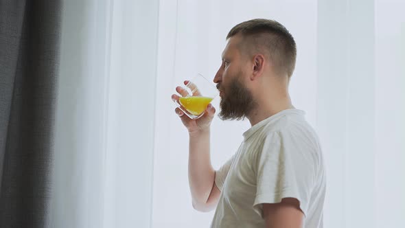 bearded man near the window drinking orange juice.  fresh squeezed orange juice alt