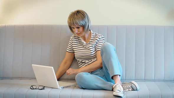 A Happy Beautiful Elderly Woman Enjoys the Good News While Looking at Her Laptop While Sitting at