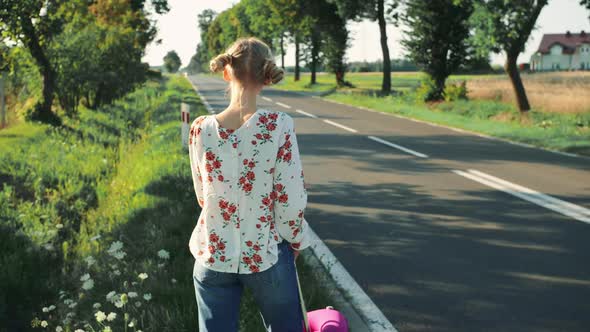 Young Beautiful Woman Hitchhiking Standing on the Road with a Suitcase