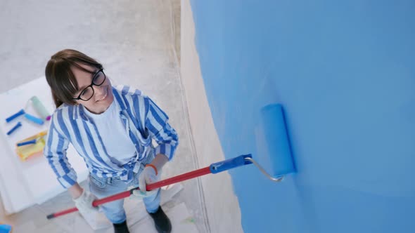 Girl Paints Wall Blue with Construction Roller in Room During Finishing Work Background of Tools alt