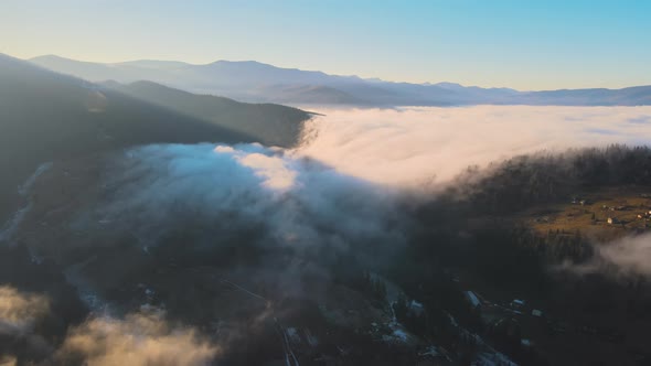 Aerial View of Vibrant Landscape of Foggy Clouds Covering Mountain Hills and Small Scattered Village alt