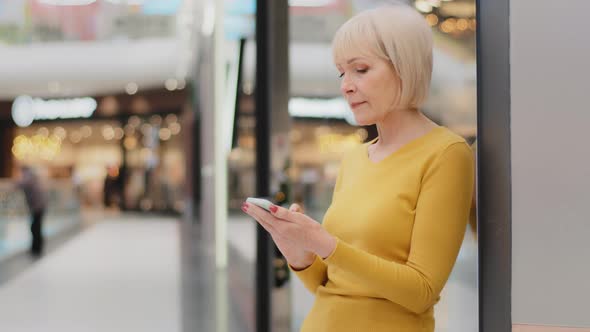 Smiling Middle Aged Mature Caucasian Woman Holding Phone Looking at Smartphone Screen Sending alt