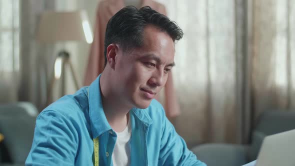 Close Up Of Asian Male Designer Working On A Laptop While Designing Clothes In The Studio alt