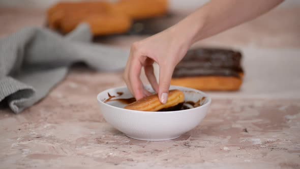 Hands dipping eclair in chocolate fondant.