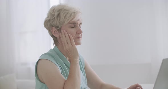 Middle-aged Woman with Migraine Is Working with Notebook in Office, Typing on Keyboard Touching alt