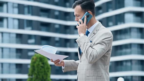 Businessman Talking On Smart Phone And Holding Business Contract In Hand