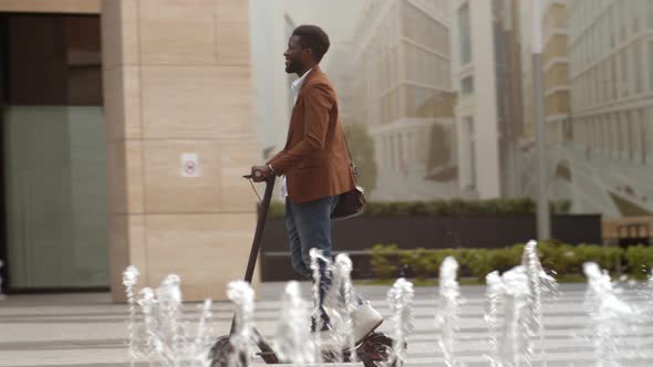 Smiling Man Riding Electric Scooter near Fountain alt
