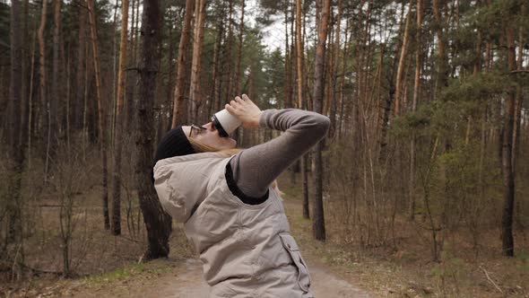 A Woman Drink Coffee and Make a Fun Dance in  Motion Next To a Pine Forest. alt