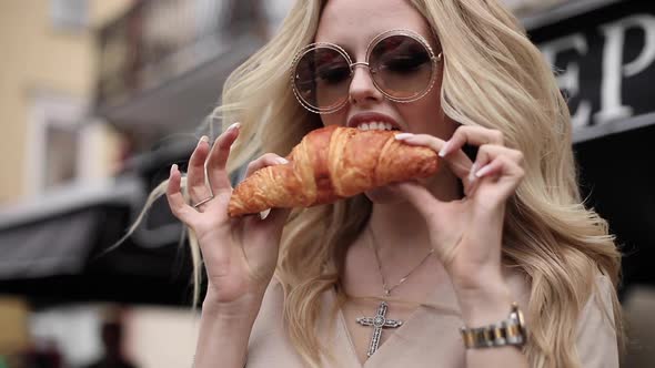 Close-up Smiling Woman Tearing Off Fresh Appetizing Croissant By Hand Having Positive Emotion