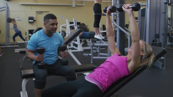 Woman lifting weights with trainer at gym