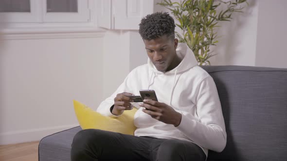 Serious Young Man Typing Card Number for Payment Via Smartphone alt