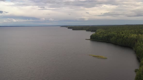 Quadrocopter flies over a lake surrounded by forest