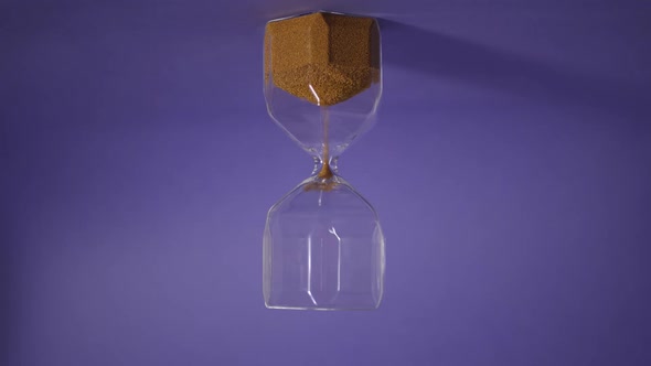 Glass Hourglass with Golden Sand on Purple Background alt