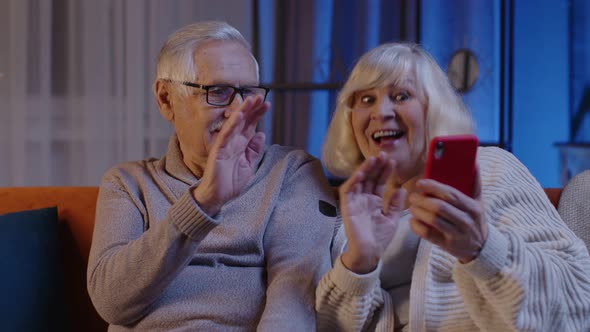 Smiling Senior Couple Grandmother Grandfather Making Video Call Online on Mobile Phone at Home Sofa alt