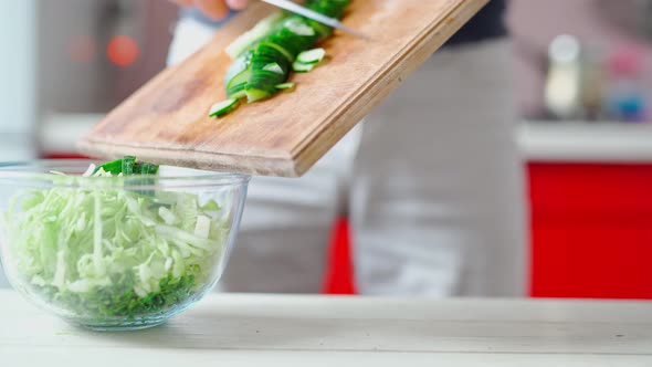 Cook Puts Cutted Cucumber From Wooden Cutboard to Transparent Glass Bowl alt
